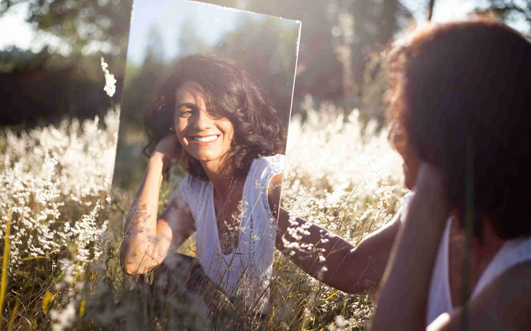 Beautiful woman looking at herself in a mirror surrounded by flowers